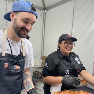 Chef and Culinary Careers Program participant slice pizza together at a food festival booth.