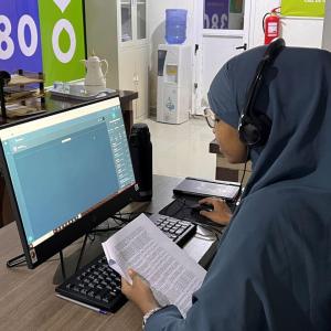 Sahra Ibrahim, a call center assistant, is wearing a headset to take phone calls while working on her computer. 