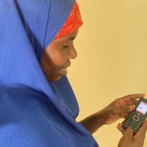 A woman holds a small cellphone in front of a yellow wall. 