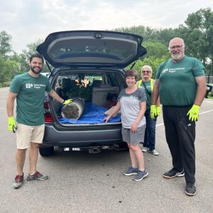 People stood next to a car that has the boot open and a plant inside