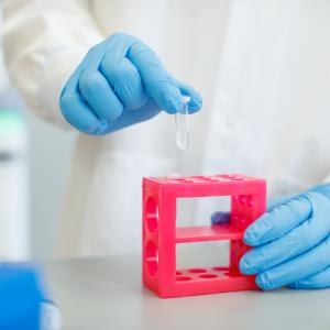 Illumina scientist; gowned and gloved removes a test tube from a rack.