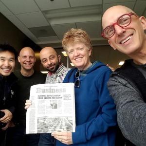 Shannon Whitmore with three men, holding a newspaper with a headline "Illumina Buys Startup"