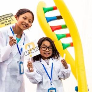 Two young female students shown in lab coats and a double helix.