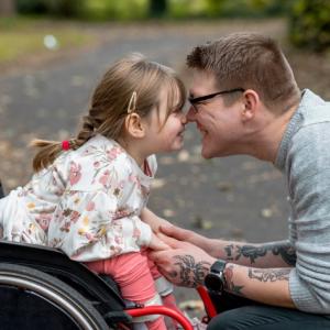 Young girl in a wheel chair with her dad hugging her.
