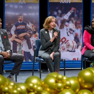 Three speakers seated on a stage, one speaking into a microphone.
