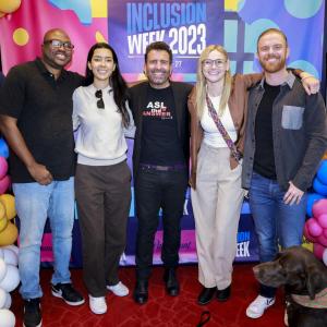 Five people posed with arms around each other. Balloons and "Inclusion Week 2023" behind them.