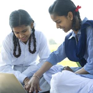 Two children outdoors under a tree looking at a laptop screen