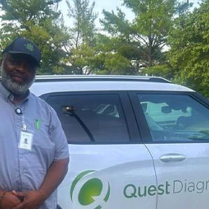 A person leaning against a white car that has the Quest Diagnostics logo on the side