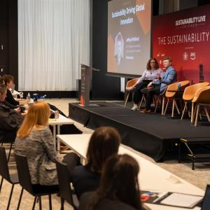 Wide shot of a fireside chat at Sustainability LIVE Chicago 205 with two people on stage and audience seated.