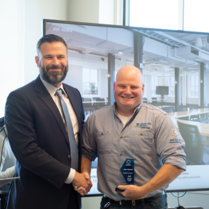 Jason and another person shaking hands as he holds an award.