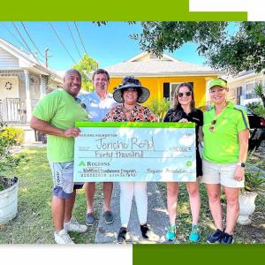 Five people holding a large check in front of a yellow house.
