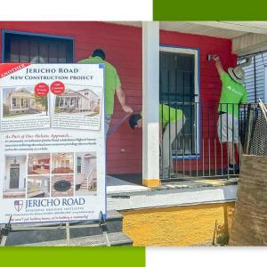 Volunteers painting a house red. A board with information in front of them.