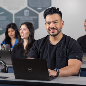 Juan Arbizu typing on a laptop in a classroom with others.