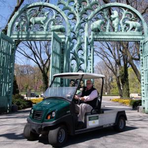 Jim Breheny, director of the Bronx Zoo, sits in one of the new electric vehicles in front of two large gates.