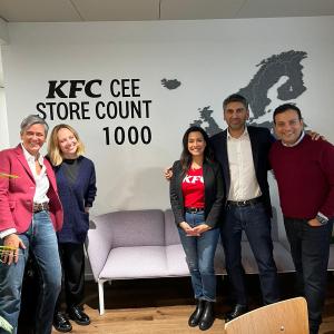 Five smiling people standing in a room with a couch and "KFC CEE store count 1000" on the wall behind them.