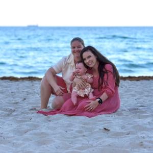 Kathryn and Emily holding their child sitting on a beach
