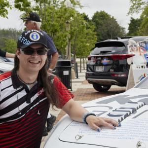 a person crouched by a car, hand on the hood
