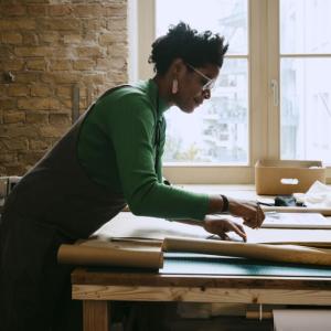 Woman shown standing at a desk reviewing paperwork.