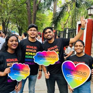 A group posed outside holding rainbow colored, shaped boards "Kohler Proud"
