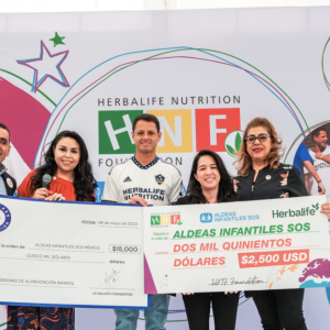 Five people in front of a large banner, holding up two checks.