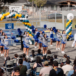 School cheerleaders performing a routine on a blue outdoor soccer court.