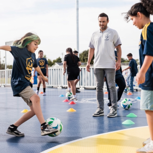 Landon Donovan watching a student practice soccer drills on a mini-pitch.