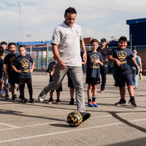 Landon Donovan kicking a soccer ball while surrounded by a group of students.