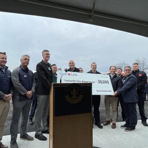 A group of people posed with a large check behind a podium outside.