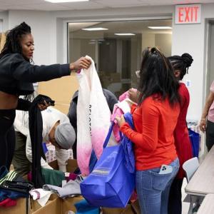 A person hands a large bag to others, small group of people looking through boxes.