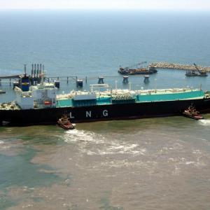 A large tanker with "LNG" on the side being pushed by smaller boats