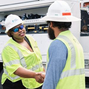 LaQuitta Ghent shaking the hand of another, both in safety wear. A repair vehicle behind them.