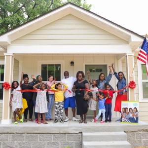Latonya and her family cutting a red ribbon in front of her new home