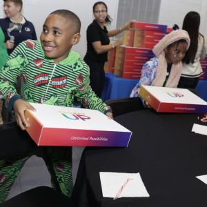 Excited children with boxes labeled "project UP". A stack of boxes behind them and a round black table in front .