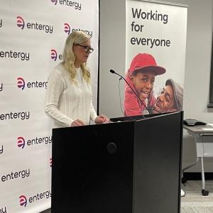 A person stood at a microphone stand, in front of an Entergy backdrop 