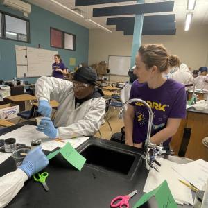 A woman in a purple SPARK™ MilliporeSigma t-shirt engages with students on science lessons. 