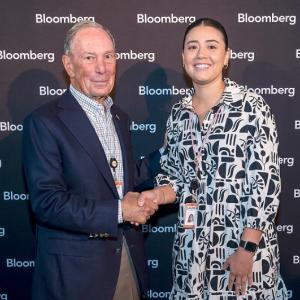 Two people shaking hands for a photo against a Bloomberg backdrop