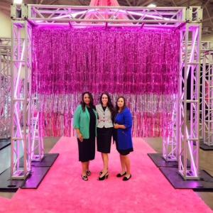 Three people posing for group picture against pink backdrop