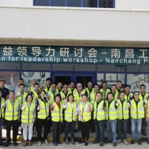 A group in front of a building, all wearing safety vests and giving 'thumbs-up'. A banner "Lean for leadership workshop - Nanchang Plant".