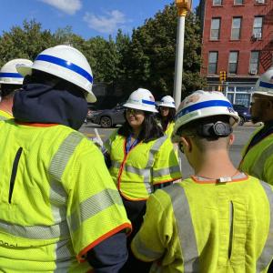 Girl stands on street corner with staff from National Grid in yellow safety vests.