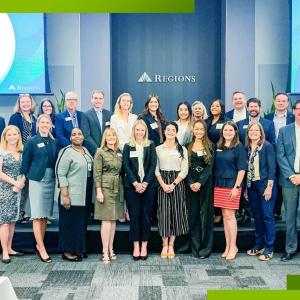 A group of interns and employees posed on a stage. Regions sign and digital screens behind them.