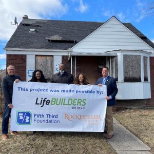 5 people holding a LifeBUILDERS sign outside a house