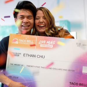 Two smiling people posed with a large check. Confetti falling around them.