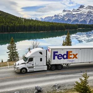 FedEx Freight truck driving past a lake with mountains in the distance