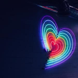A rainbow heart in neon lights on a dark wall.
