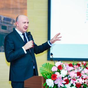 An event speaker holding a microphone while stood next to a projector board 