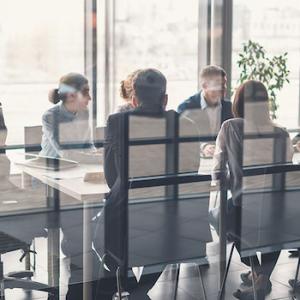 Group of eight men and women of diverse ethnic backgrounds are sitting at a boardroom table.