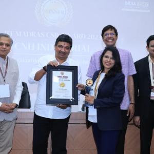 Five smiling people posed, two holding a plaque.