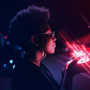 Black person with glasses and large earrings smiling with eyes closed, holding glowing pink lights