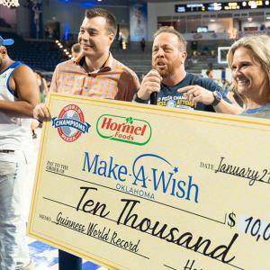 Three people holding up a giant check to Make A Wish for $10,000. Standing on a basketball court.