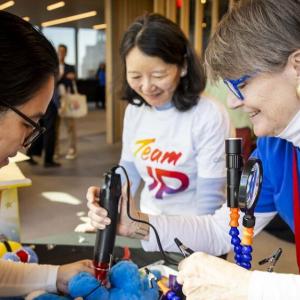 Three people stood around a table helping to modify toys for children with disabilities 